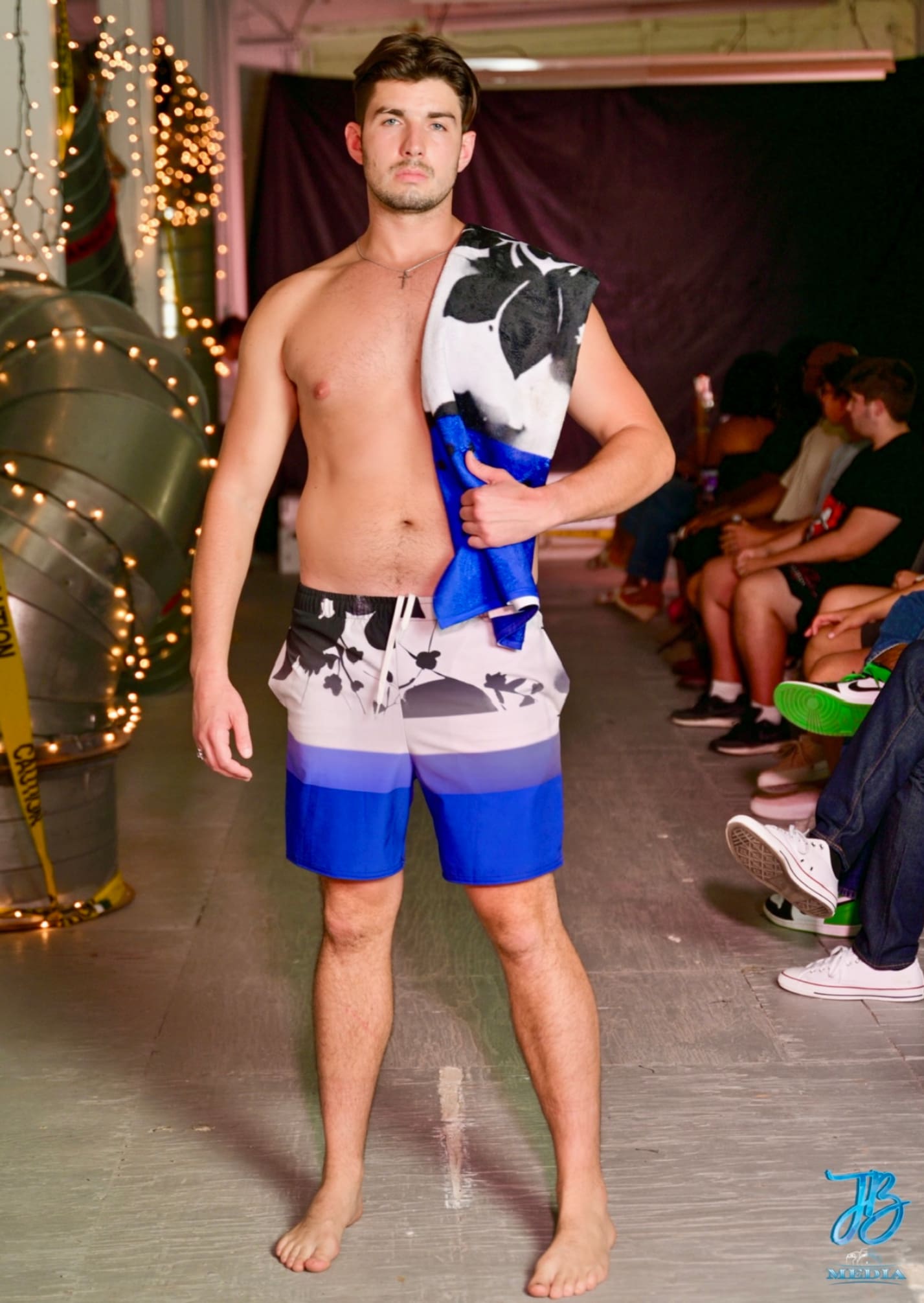 A man in swim trunks holding a blue and white umbrella.