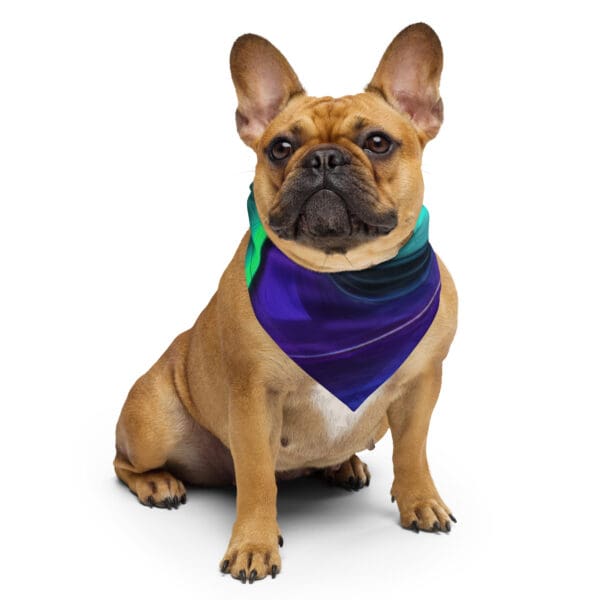 A brown dog sitting on the ground wearing a purple and blue bandanna.