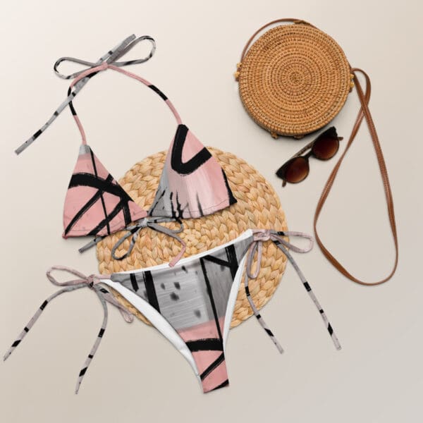 A pair of pink and black bikini bottoms next to a straw bag.