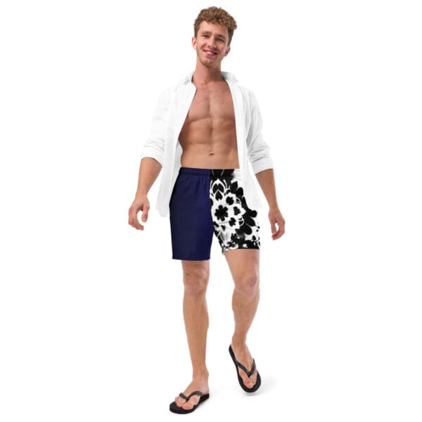 A man in black and white swim trunks standing next to a wall.