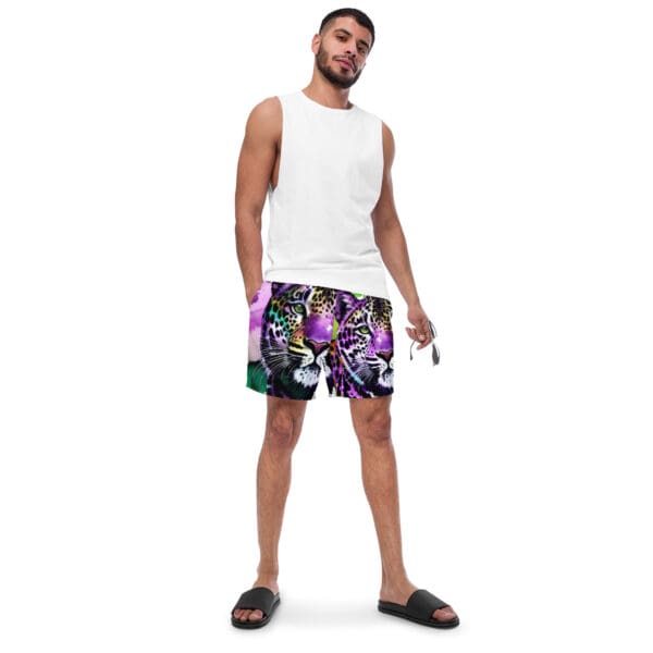 A man standing in front of a white wall wearing black and purple shorts.