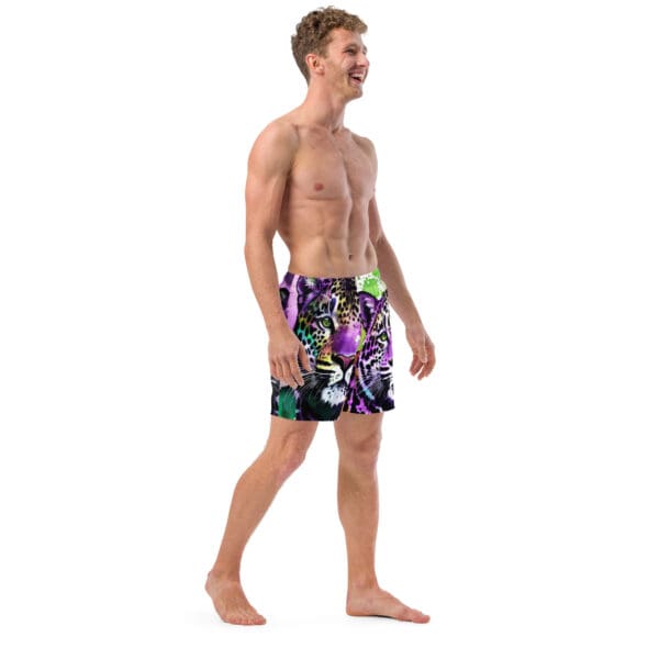 A man in swim trunks walking on the beach.