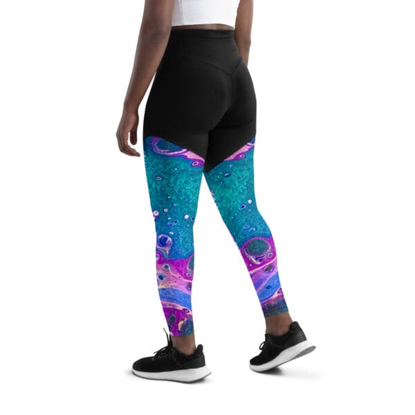 A woman wearing black and blue leggings with pink, purple and green designs.