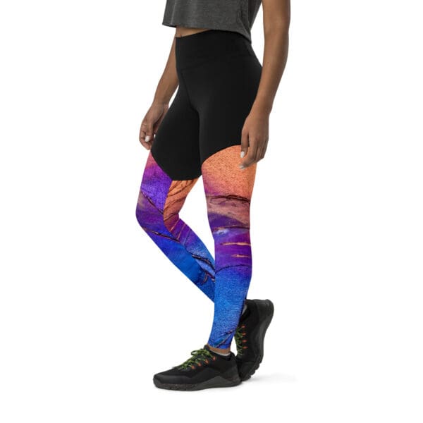 A person wearing colorful leggings standing next to a black wall.