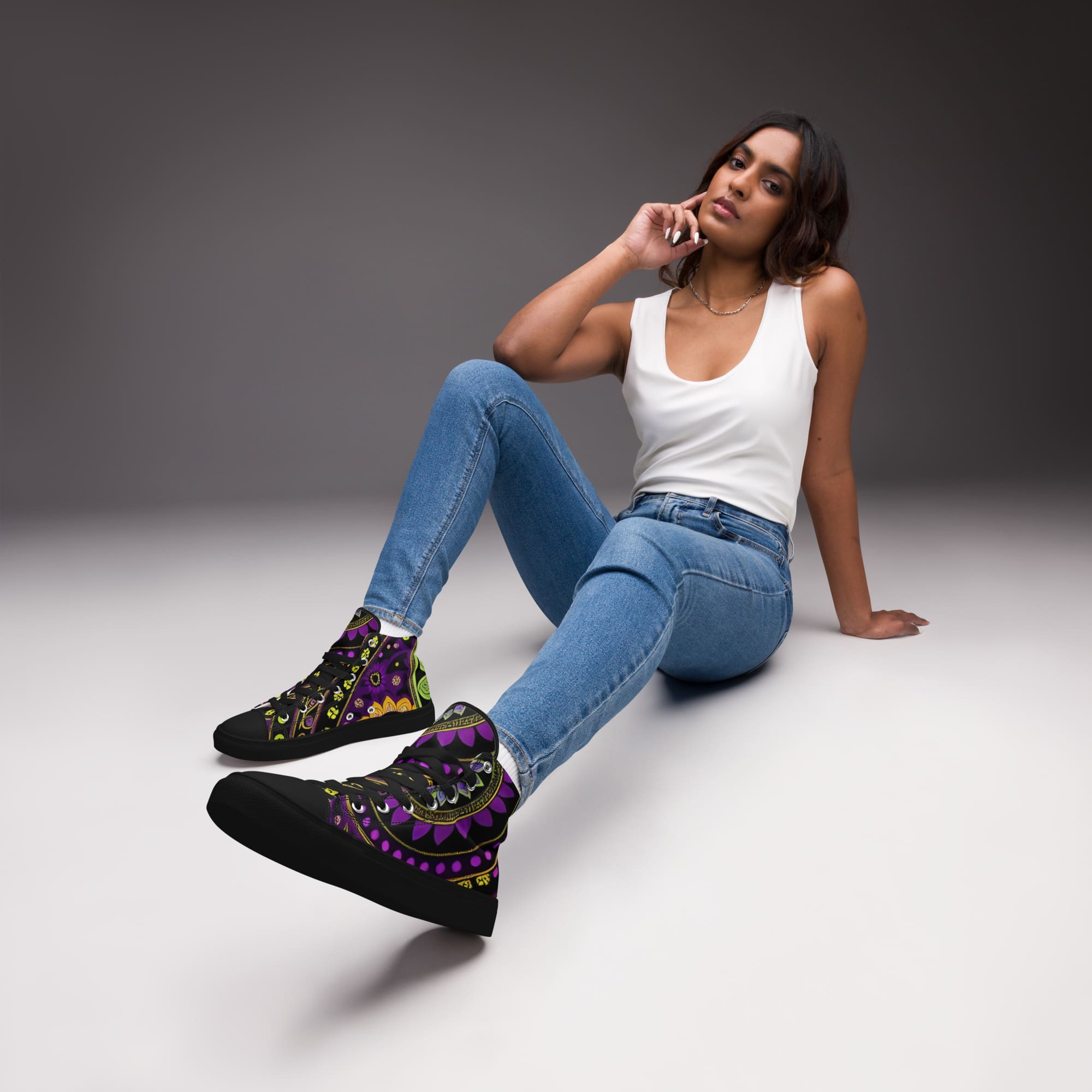 A woman sitting on the ground wearing jeans and sneakers.